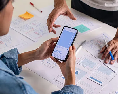 Designers reviewing a mobile app prototype over paper UX wireframes